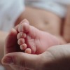 A close-up of a baby's foot resting gently in an adult's hand, with the baby's soft skin and tiny toes in focus.